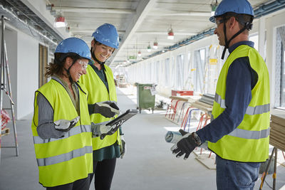 Smiling male and female architects discussing over digital tablet at construction site