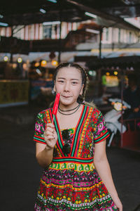 Portrait of smiling young woman eating flavored ice while standing outdoors