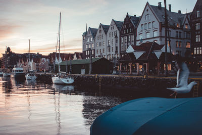 Sailboats moored on harbor by buildings against sky during sunset