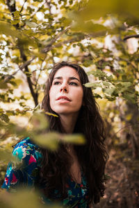 Young woman looking away against trees