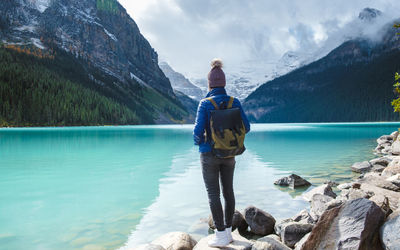 Rear view of woman standing on rock by lake