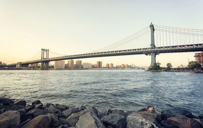 Low angle view of manhattan bridge over river against clear sky during sunset