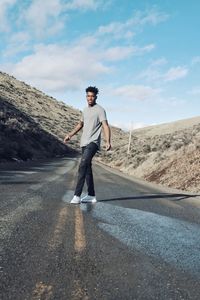 Full length portrait of young man standing on road against sky