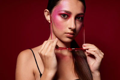 Close-up of young woman applying make-up against black background