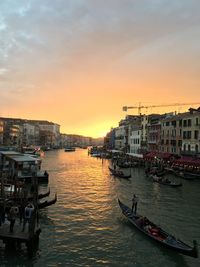 Boats moored in canal by buildings against sky during sunset