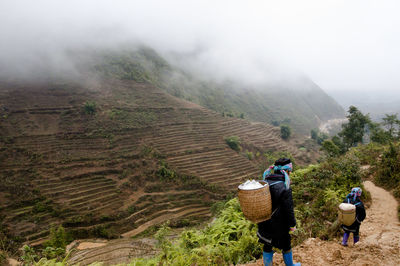 Rear view of people walking on landscape against sky during foggy weather