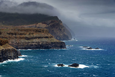 High angle view of rocky coastal feature against clouds