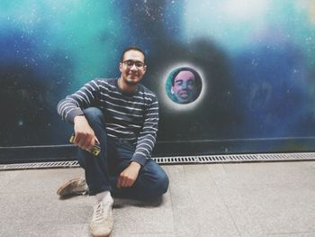 Portrait of smiling young man sitting against painting on wall