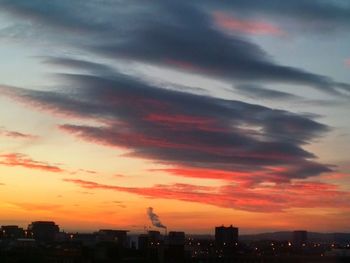 Silhouette buildings against dramatic sky during sunset