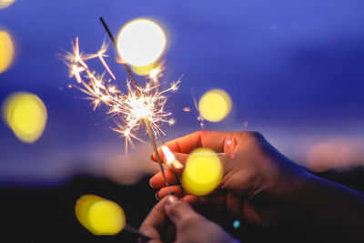 Cropped hand of woman holding lit sparkler at night