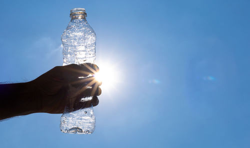 Hand holding glass bottle against blue sky