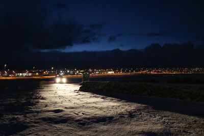 Illuminated city by sea against sky at night