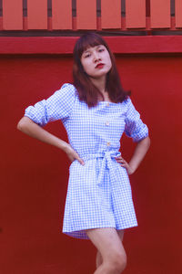 Young woman looking away while standing against red wall