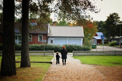 Rear view of grandson sitting on bicycle by woman standing on dirt road by trees