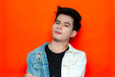 Portrait of young man looking away against orange background