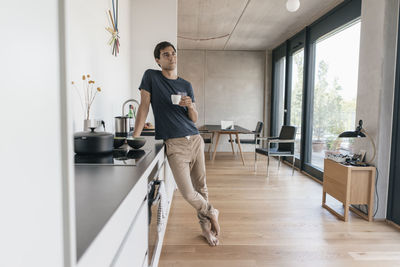 Young man holding cup of coffee in kitchen at home