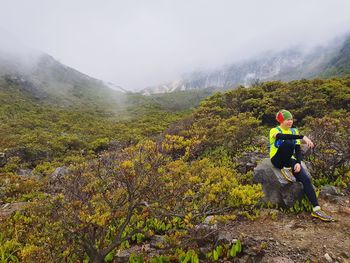 Man sitting on rock at gunung gede pangrango national park during foggy weather