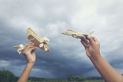 Cropped hands of people holding model airplane against cloudy sky