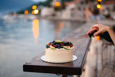 Cropped hand of people cutting cake by river
