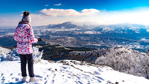 Girl standing on snowcapped mountain against sky