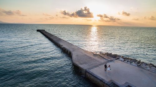 High angle view of couple walking on pier by sea against sky during sunset