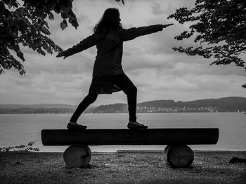 Rear view of woman standing on shore against sky