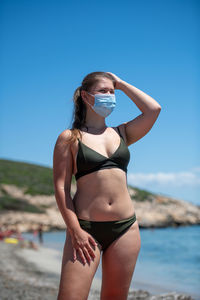 Full length of young woman standing on beach against clear blue sky