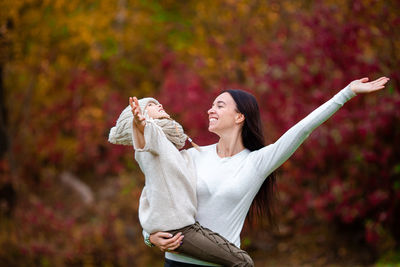 Woman with arms raised standing against autumn leaves