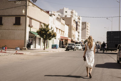 Woman walking on road along buildings