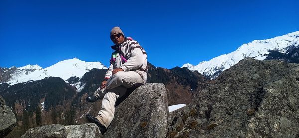 Man wearing sunglasses sitting on rock against nowcapped mountains