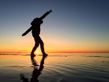 Silhouette man standing on beach against sky during sunset