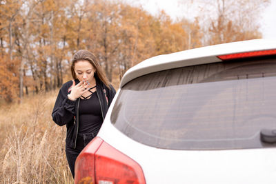 Woman smoking while standing by car in forest