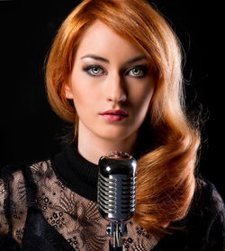 Portrait of redhead young woman singing in microphone against black background