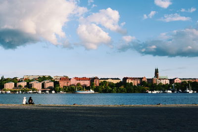 View of buildings by river against cloudy sky