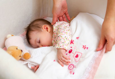 Cropped hands of woman touching baby girl sleeping in crib at home