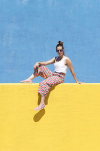 Trendy woman sitting on yellow wall while looking camera