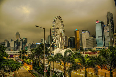 Ferris wheel by modern buildings in city against sky