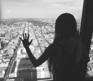 Rear view of woman looking through window with cityscape in background