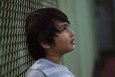 Close-up of cute boy leaning on chainlink fence