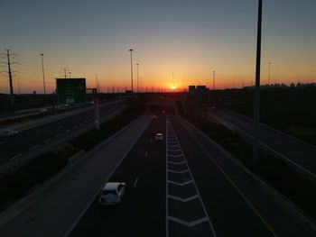 Vehicles on road against sky during sunset
