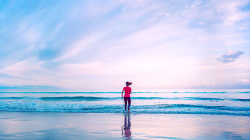 Rear view of woman standing at beach against sky