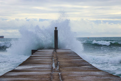 View of waves splashing on pier against sky