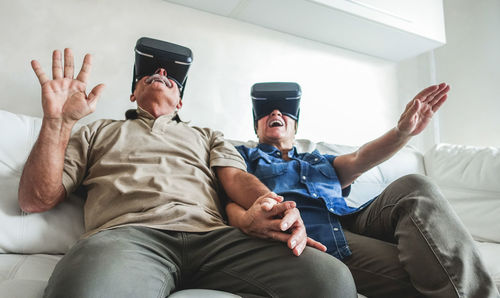 Low angle view of senior couple looking through virtual reality simulators while sitting on sofa at home