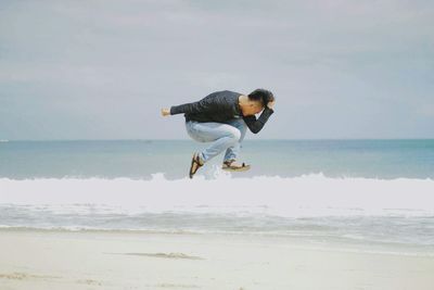 Man jumping at beach against sky