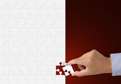Cropped hand arranging jigsaw puzzle over red background