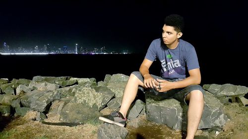 Young man sitting on rock at night