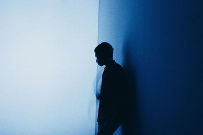 Side view of man leaning on blue wall against white background