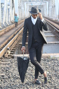 Man with umbrella walking on railroad track