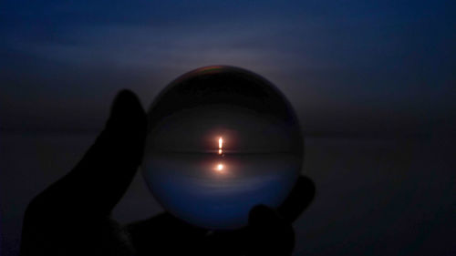 Silhouette hand holding ball against sky during sunset