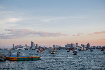 Boats in sea by buildings against sky during sunset